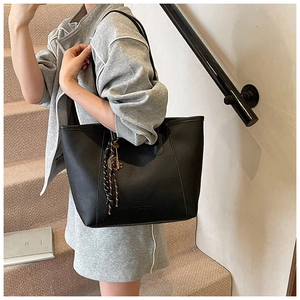 Close-up of black litchi grain tote bag featuring a decorative key and tassel charm detail