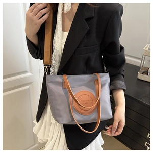 Detail of grey nylon tote bag with brown adjustable shoulder strap and logo patch