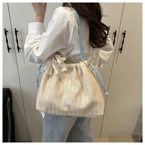 Detail einer Strohtasche mit blauem Kordelzug und einer großen weißen Spitzenschleife