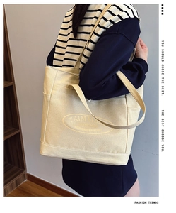 Detail of a large beige canvas tote bag with side pocket and shoulder strap on a model