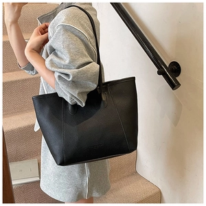 Detail of black lychee-grain tote bag with thin straps and embossed logo on casual model