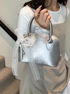 Silver shell-shaped handbag with lace bow and pearl charm carried by a model