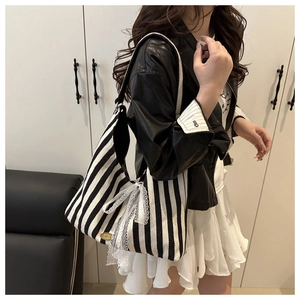 Detail of striped canvas tote bag with lace bow and oval metal logo on the side