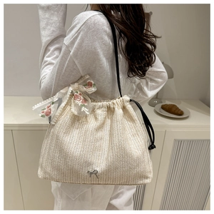 Detailansicht der gewebten Strohtasche mit weißer Spitzenschleife und Metallanhänger
