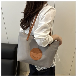 Detail of grey nylon tote bag with leather straps worn by model in minimalist setting