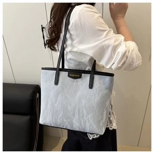 Detail of grey pleated tote bag featuring fashion logo plaque and black leather handles