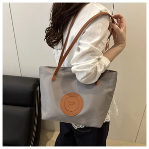 Detail of grey nylon tote bag with brown leather straps and fashion bags logo patch