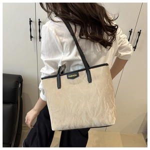 Detail of off-white tote bag with black trim and gold FASHION label on textured fabric