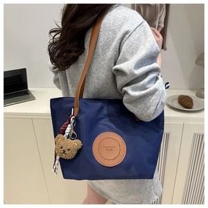 Navy nylon tote bag with leather straps and cute bear charm shown on model shoulder
