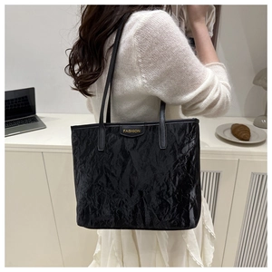 Detail of a black pleated tote bag with golden fashion plate and leather handles
