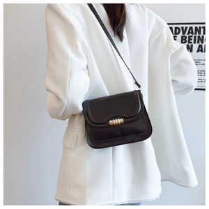 Close-up of black leather crossbody bag with wavy edge and golden lock on white blazer