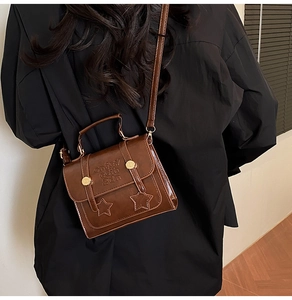 Detail einer dunkelbraunen Ledertasche mit Sternnähten und Griff, getragen von einem Modell