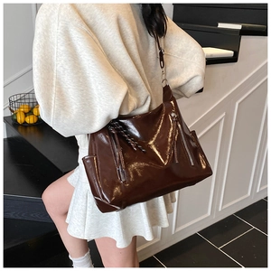 Detail of dark brown glossy tote bag with dual side zippers and woven tassel charm