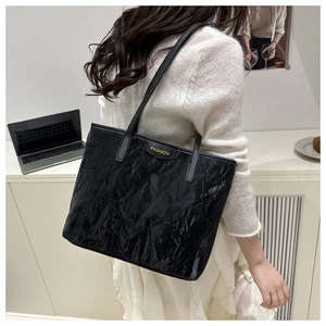 Detail of black tote bag featuring gold FASHION plaque and pleated texture finish
