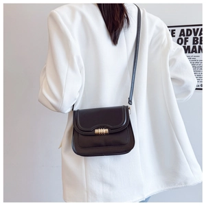 Detail of minimalist black crossbody bag featuring a round golden buckle on white blazer