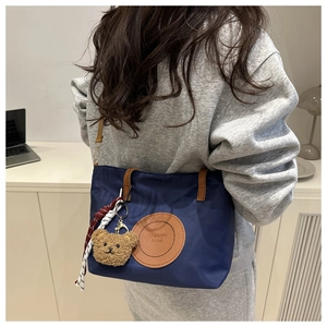 Rear view of model wearing a dark blue nylon tote bag with brown leather handles and bear charm