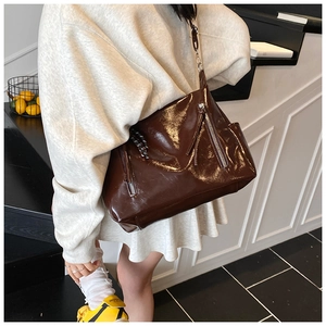Detail of dark brown patent leather tote bag with glossy finish and silver zippers