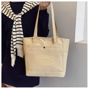 Detail of canvas tote bag showing metal snap pocket and printed logo typography