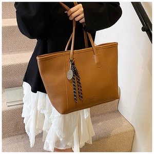 Detail of brown faux leather tote bag with metal tennis racket charm and tassel decor