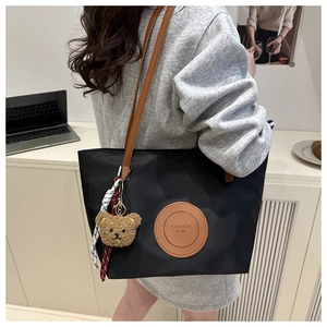 Detail of black nylon tote bag with brown leather straps and cute bear charm accessory