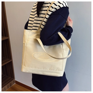 Detail of beige canvas tote bag showing the front pocket and logo in a lifestyle setting