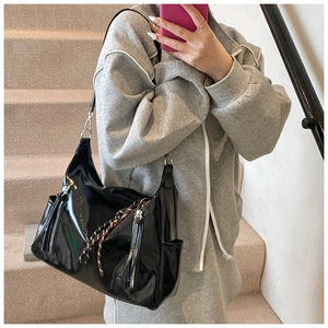 Detailed view of large black patent leather tote with decorative fringe and braided zipper cord