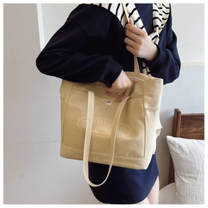 Detailed view of cream canvas tote bag showing clear texture and front pocket stitching