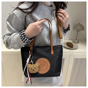 Detail of black nylon tote with leather patch, teddy bear charm and woven strap