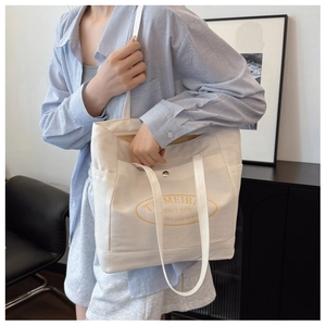Detail of white canvas tote bag with orange logo worn by model in minimalist setting
