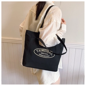 Détail du sac cabas en toile noire montrant la poche latérale et la bandoulière renforcée