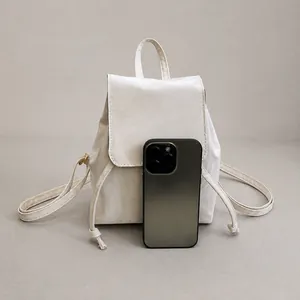 Mini white drawstring backpack size comparison with a smartphone on textured fabric