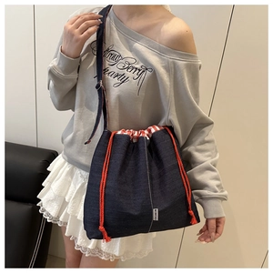 Détail d'un sac seau en denim bleu avec cordon rouge et doublure en tissu à carreaux