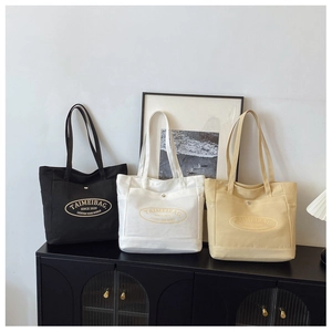 Detailed view of three canvas tote bags in black, white, and beige with brand logo
