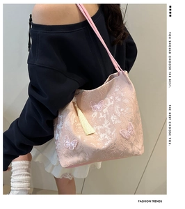 Detail of pink jacquard tote bag with butterfly embroidery and tassel hanging on a model