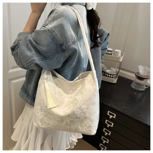 Detail of white lace tote bag featuring embroidered butterfly patterns and tassel charm