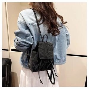 Model view of black wrinkled fabric backpack with flap and drawstring in minimalist room