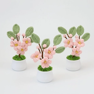 Trois plantes en pot de fleurs de pêcher crochetées à la main avec feuilles dans des pots blancs