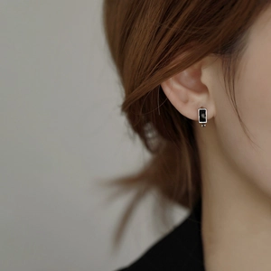Close-up of black rectangular stud earring with silver bezel on a female model