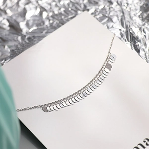 Close-up of a silver tassel anklet with dangling round sequins on white background