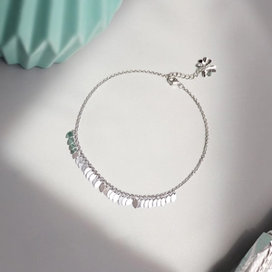 Detailed view of silver leaf tassel anklet with four-leaf clover charm on grey background