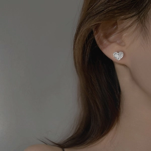 Détail de boucles d'oreilles cœur argenté avec texture lave portées par un modèle
