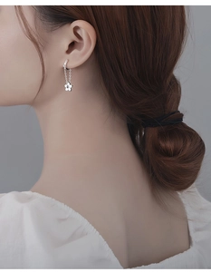 Detail of silver S925 flower drop chain earrings worn by a model in a close-up shot