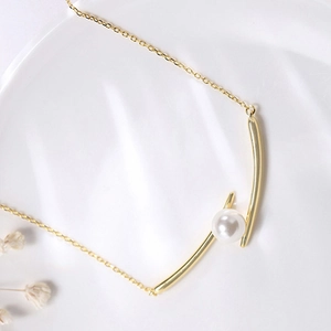 Macro detail of gold necklace featuring minimalist irregular metal bars and white pearl