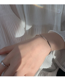 Close-up of minimalist silver wavy open bangle and sparkling diamond ring on a wrist