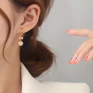 Elegant gold bow earrings with cat eye stone and cubic zirconia, shown on a model's ear