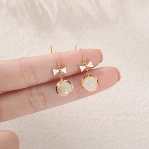 Elegant gold bow earrings with cat eye stone beads and circular rings on white plush