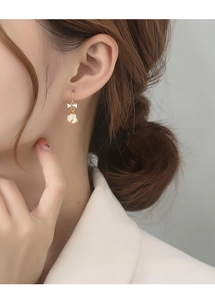 Close-up of golden bow earrings with cat's eye stones worn by a female model