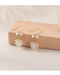 Close-up of golden bow earrings with cat eye stone and diamonds on a wood stand