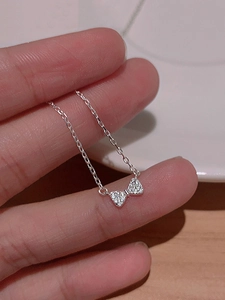 Macro detail of a silver bow necklace pendant with micro-paved zircons on a delicate chain