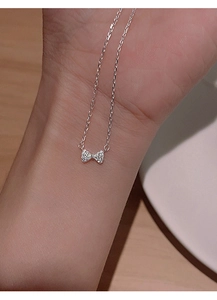 Close-up of a silver bow necklace with micro-pave zircons worn on the wrist for detail